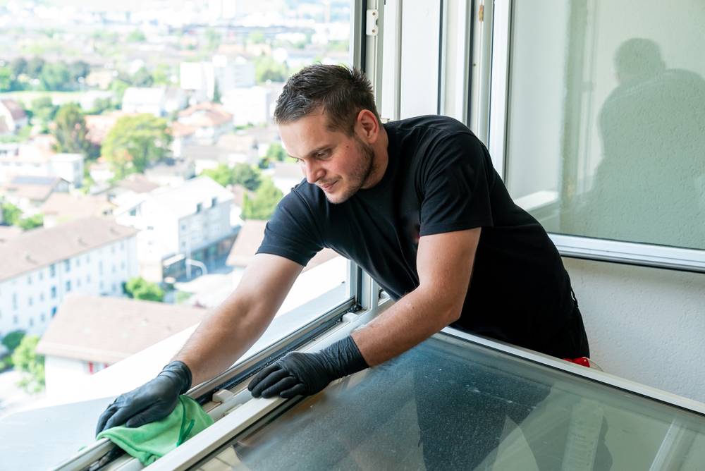 GDM-Mitarbeiter reinigt einen Fensterrahmen, im Hintergrund der Blick über die Stadt