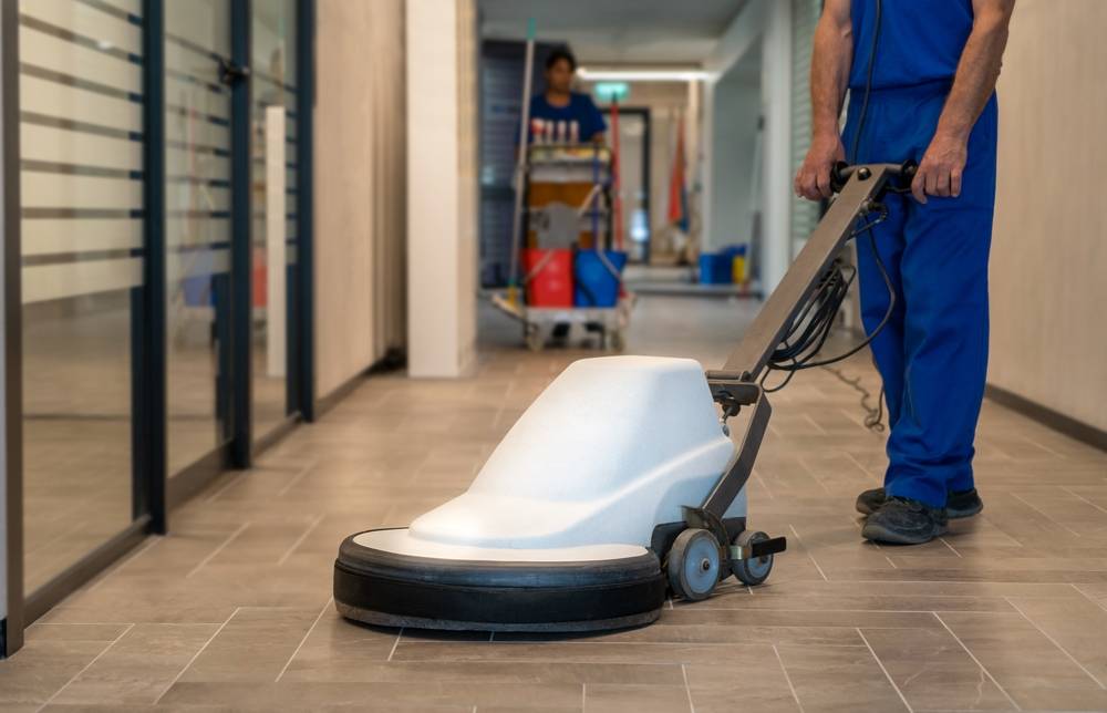 Reinigungskraft mit Einscheibenmaschine im Flur eines Bürogebäudes